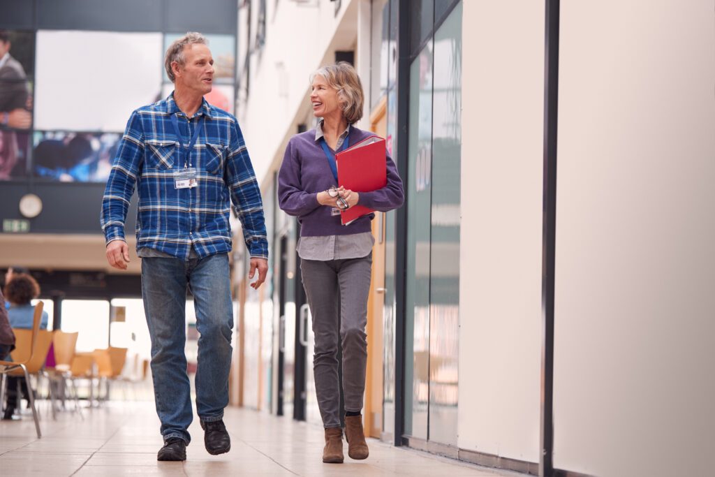 Two,Mature,Students,Or,Teachers,Walking,Through,Communal,Hall,Of